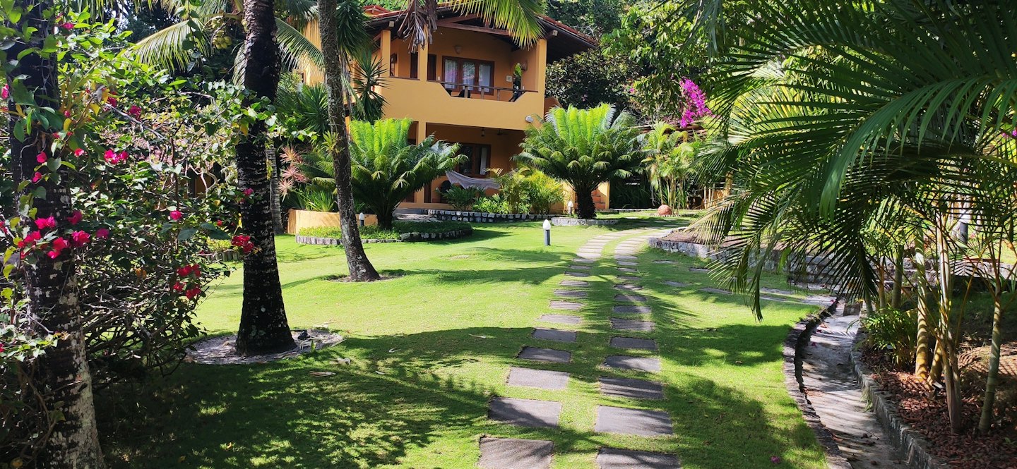 A yellow tropical house stands surrounded by lush palm trees.