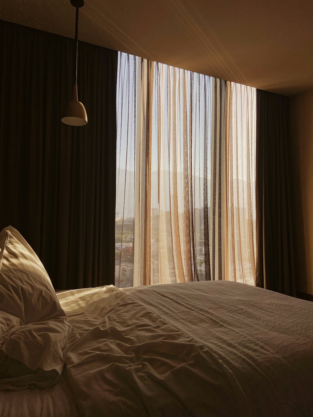 Sunlit bedroom with unmade bed and city view windows.