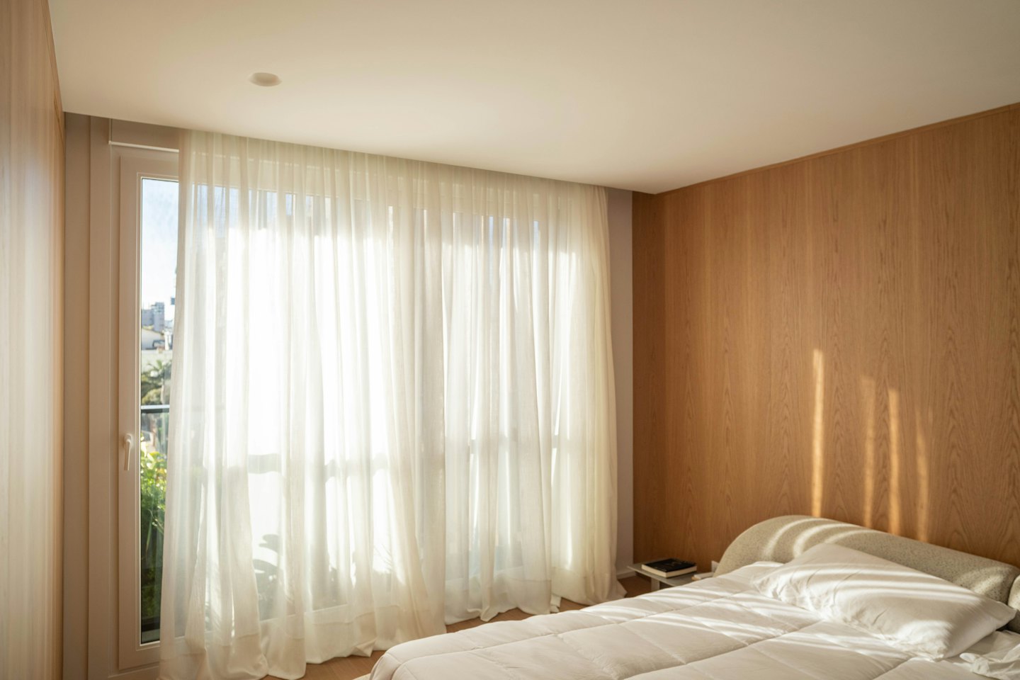 Bedroom with a made bed and sunlight streaming through a window.